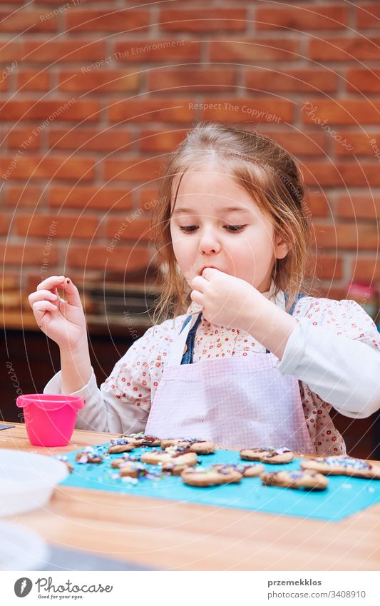Kid taking part in baking workshopLittle girl tasting cookie baked oneself. Decorating her baked cookies with colorful sprinkle and icing sugar. Kid taking part in baking workshop. Baking classes for children, aspiring little chefs. Learning to cook