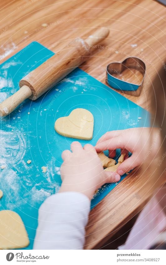 Little girl cutting the dough to heart shapes for the cookies. Kid taking part in baking workshop. Baking classes for children, aspiring little chefs. Girls learning to cook. Combining and stirring prepared ingredients. Real people, authentic situations