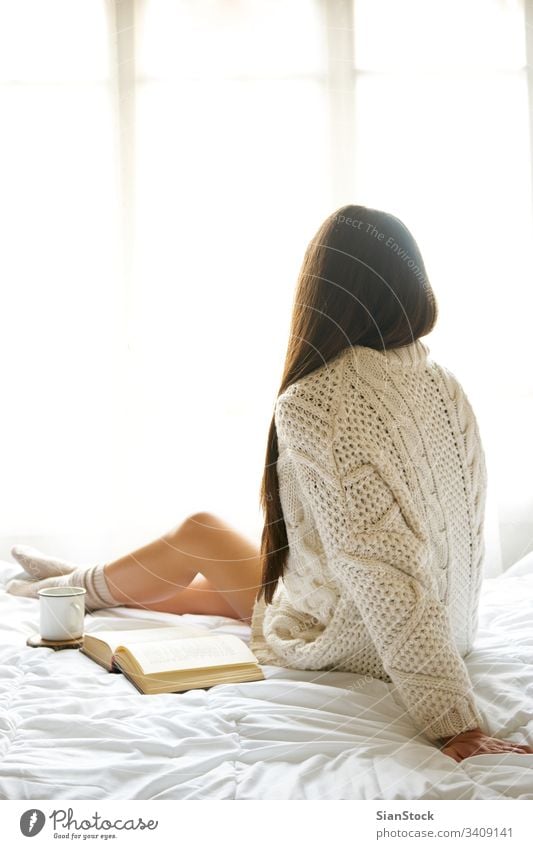 Soft photo of a woman on the bed with an old book and a cup of