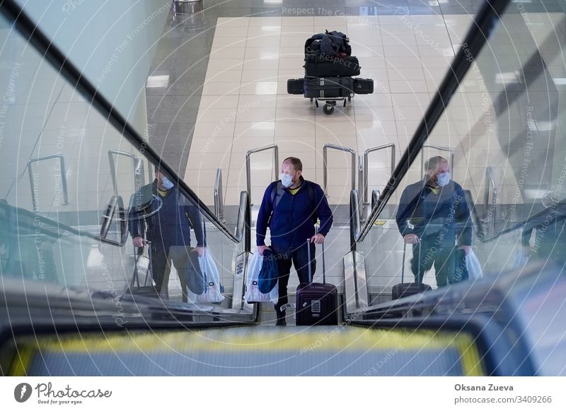 European redbeard man in  blue jacket, rises on an escalator, has protective disposable medical mask in airport. 2019-ncov afraid backpack china corona