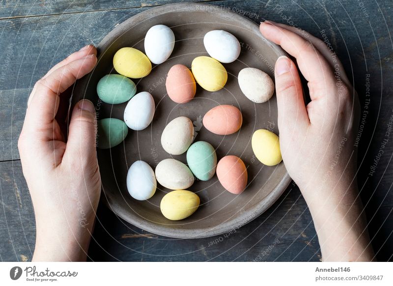 Hands holding stylish pastel painted easter eggs in ceramic grey plate on vintage old wooden background, Happy Easter holiday spring traditional symbol food