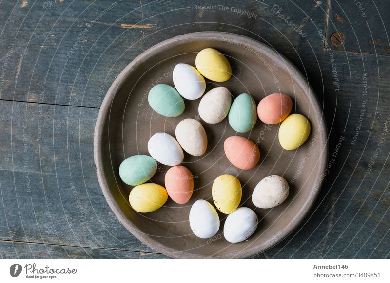 Grey Ceramic Plate with painted Easter Eggs of pastel colors on vintage wooden background. Happy Easter card concept, minimalistic design, top view spring