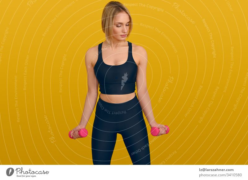Young blond woman with dumbbells on yellow active attractive background beautiful black body clothes copyspace exercise fitness gymnastics hand hands health