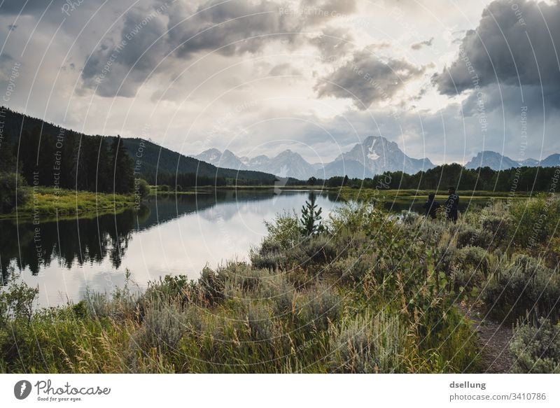 Mirror-smooth lake with green forests on the banks and steep snow-covered mountains in the background Authentic National Park Yellowstone National Park Sky