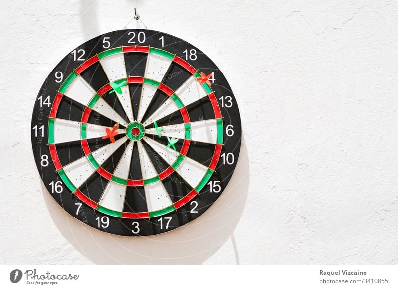 Diana with its green and red nailed darts, hanging on the white wall illuminated by the sun. target dartboard game sport isolated competition center success