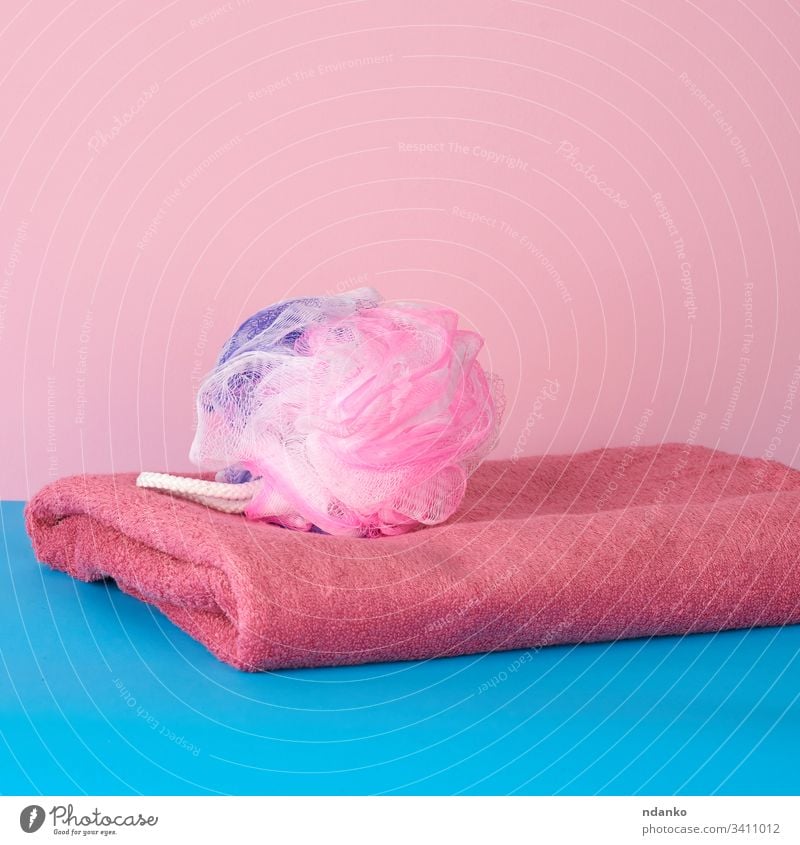 stack of pink folded towels and a plastic washcloth on a blue background bath bathroom beauty body bright care clean closeup color colorful cotton domestic dry