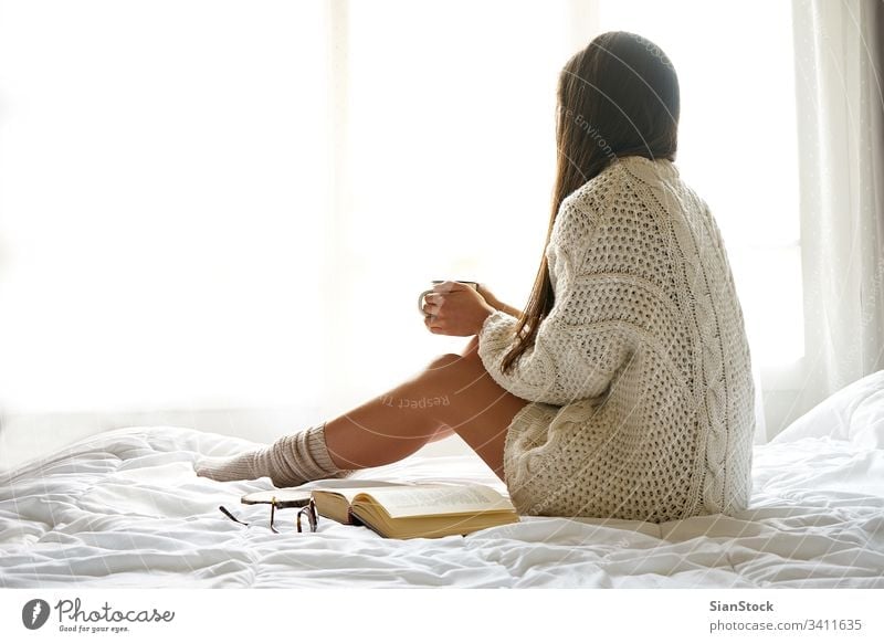 Soft photo of a woman on the bed with an old book and a cup of coffee Bed Woman Reading Window view lazy Sunday Winter Coffee Cup Tea Morning Girl Home