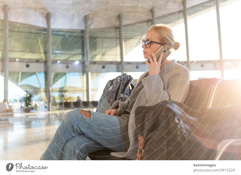 Female traveler talking on her cell phone while waiting to board a plane at departure gates at airport terminal. female woman business flight baggage luggage
