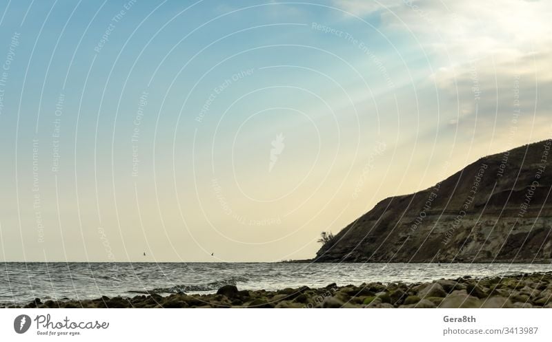 seascape with autumn sky beach blue clouds evening horizon mountain nature rock season shore stones sun rays sunset water waves yellow