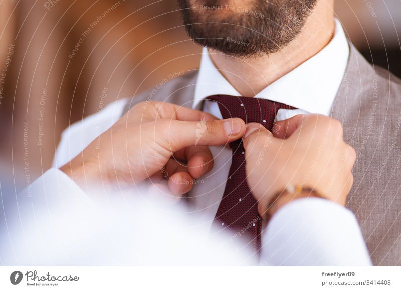 Closeup of two hands helping with the tie to a groom at his wedding suit person male decoration day vest happy floral blooming bow flower closeup engagement