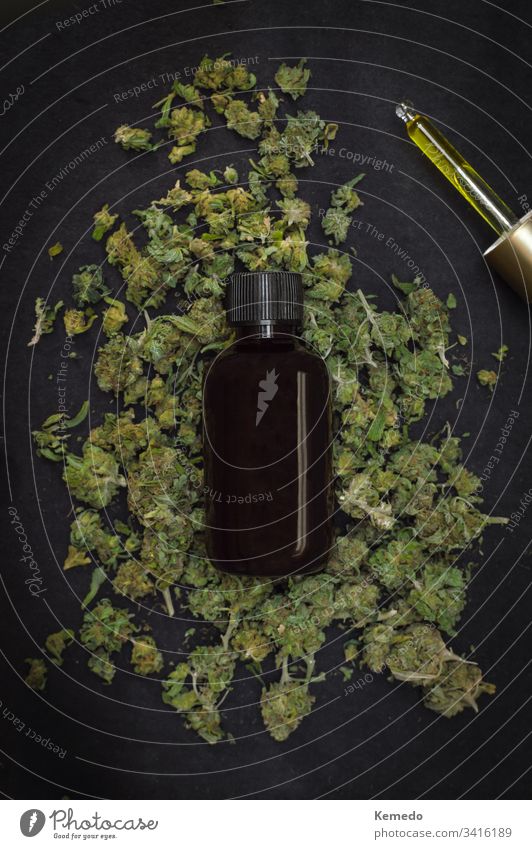 Mountain of marijuana buds with a bottle of CBD make with cannabis on top isolated on black background. CBD or cannabidiol product. cbd Cannabidiol oil weed