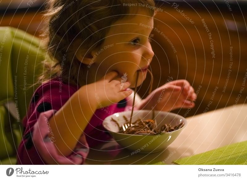 Curly little girl with an appetite eats buckwheat noodles, spaghetti. The concept of good appetite, delicious homemade food. adorable baby black blue childhood