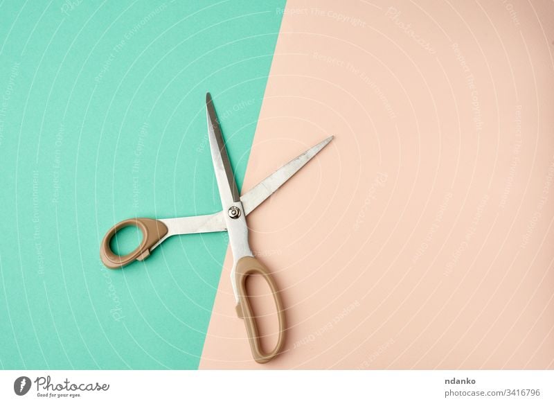 metal scissors with a plastic handle on a green-beige background open shape sharp shiny single steel tool tailor closeup professional instrument stainless paper