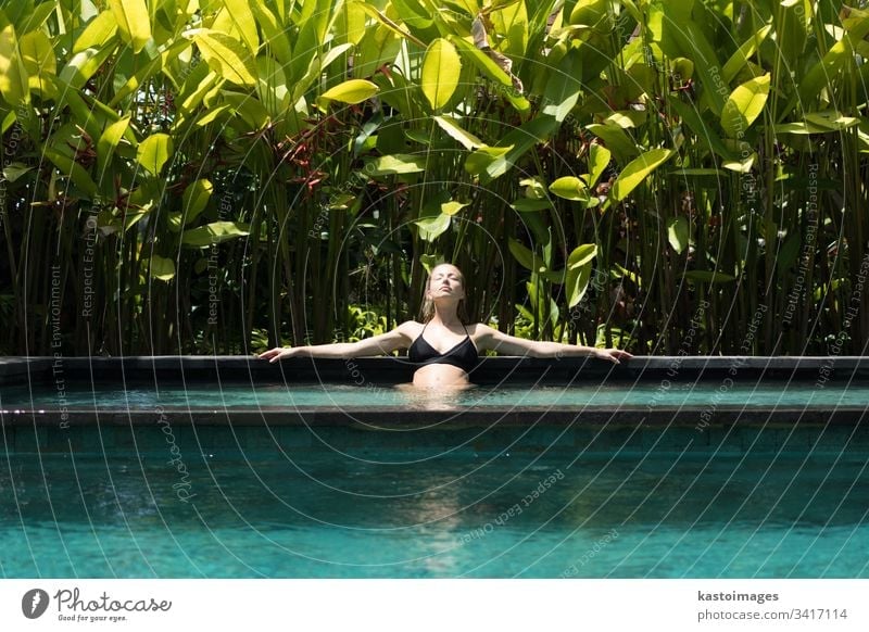 Sensual young woman relaxing in outdoor spa infinity swimming pool surrounded with lush tropical greenery of Ubud, Bali. wellness water nature beauty beautiful