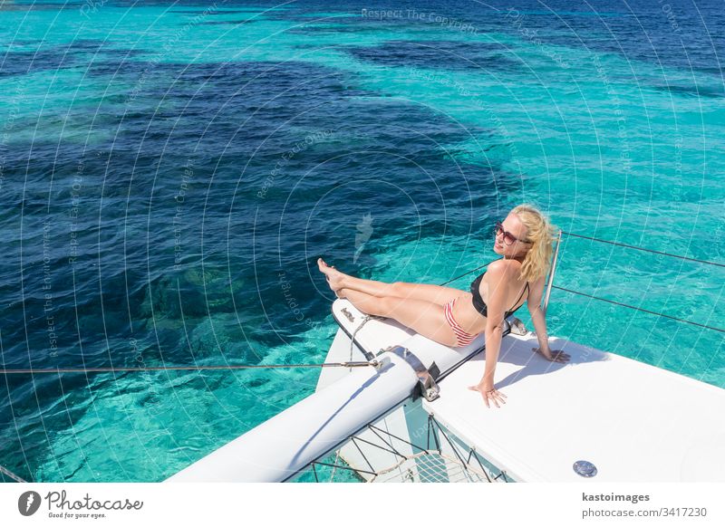 Woman relaxing on a summer sailing cruise, sitting on a luxury catamaran near picture perfect white sandy beach on Spargi island in Maddalena Archipelago, Sardinia, Italy.