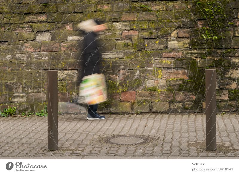 Human or alien with colorful plastic bag walks in front of dirty wall Motion blur Human being Going Wall (building) frowzy Plastic bag variegated Man Pole