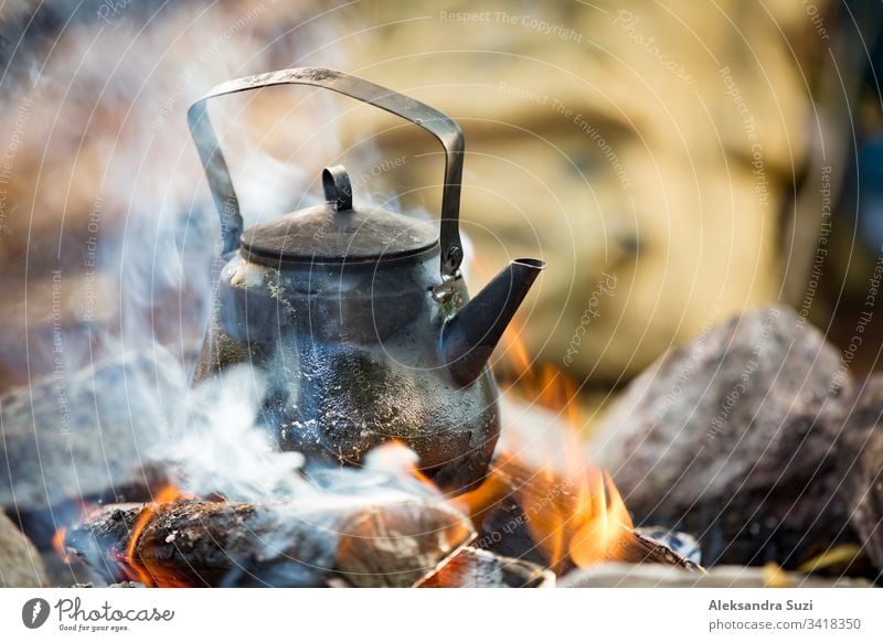 Man and woman making coffee in big kettle on campfire in forest on shore of  lake, making a fire, grilling. Happy couple exploring Finland. Scandinavian  landscape. - a Royalty Free Stock Photo