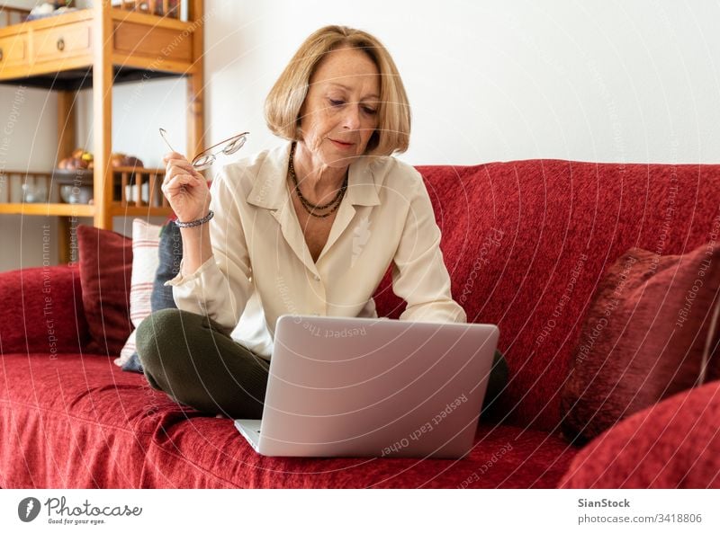 Elegant mature woman using computer at home elderly lady aged beauty wellbeing carefree comfort attractive comfortable casual blond relaxed middle-aged leisure