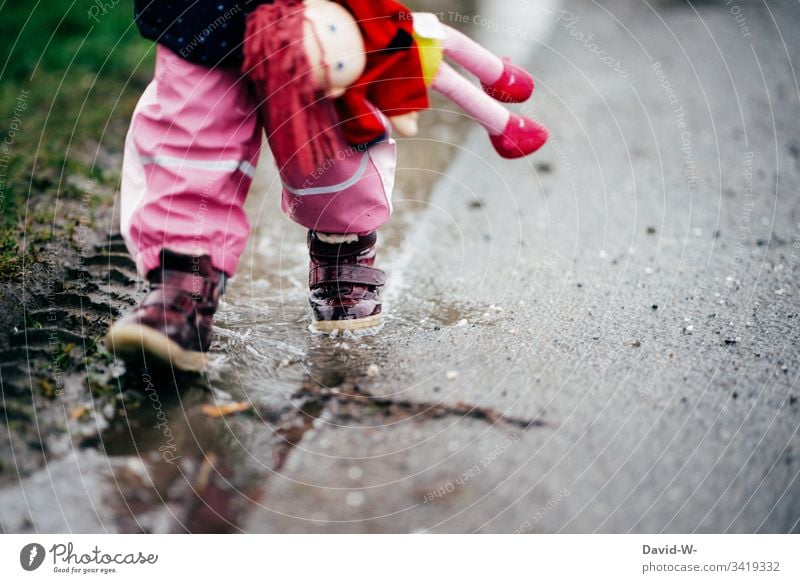 girl child runs with doll through puddle along a street Girl Street Puddle Wet Dangerous car traffic Walking Insecure Child Toddler peril Bad weather Autumn