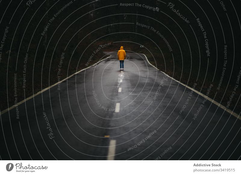 Unrecognizable man walking on lonely road in autumn forest nature rain way tree season weather empty casual yellow coat jacket freedom countryside asphalt scary