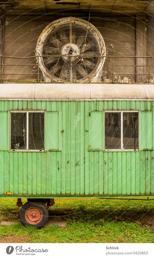 Old green construction trailer in front of a large industrial fan Site trailer Green Industrial fan Industry Fan dirt Grass Meadow Wheel Red Window