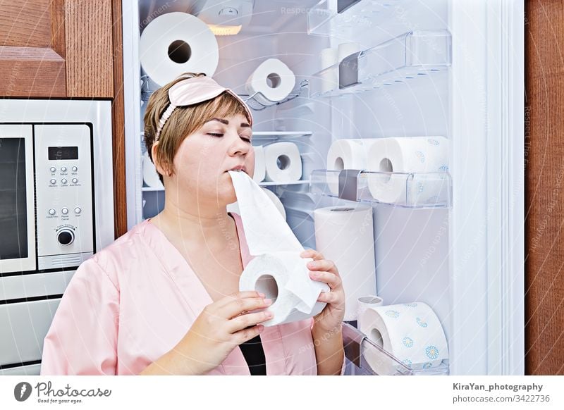 Woman in pajamas greedily eats toilet paper near the fridge filled with wc-paper night craving coronavirus woman covid-19 household hygienic tissue towel