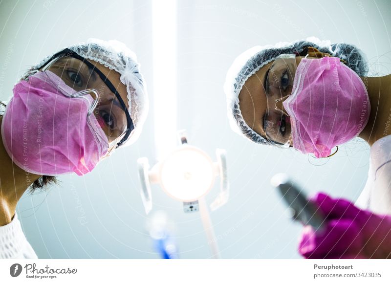 Bottom view of two women dentists in surgical mask holding tools and looking at camera dental operation females dentists office surgery doctor equipment man