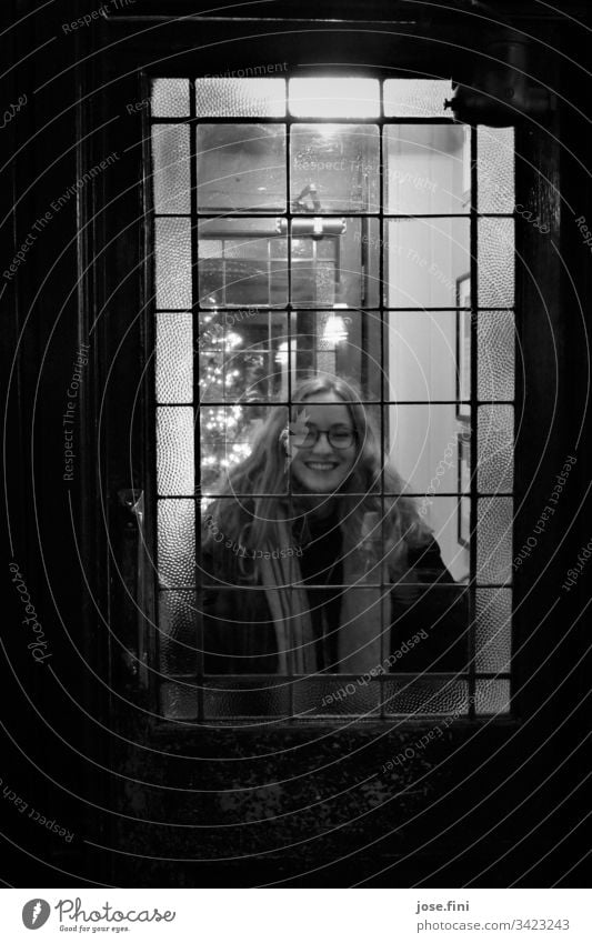 Young woman behind a glass door laughs into the camera Portrait photograph Feminine Happiness Smiling Retro Looking Lifestyle Looking into the camera youthful