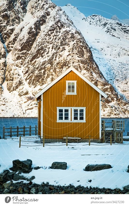 Small yellow house by the fjord in front of snow-covered mountains North Relaxation Winter vacation Ocean Snow Central perspective Environment Vacation & Travel