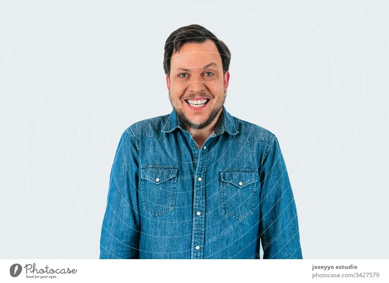 Portrait of young man smiling and looking at camera with one eyebrow raised. Denim shirt and isolated gray background. 30-40 years Raise the eyebrow absurd