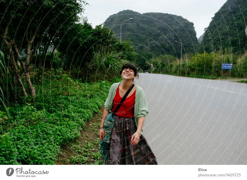 A young woman in colourful clothes walking along an empty street in Asia and smiling Woman variegated tourist Tourism South East Asia Joie de vivre (Vitality)