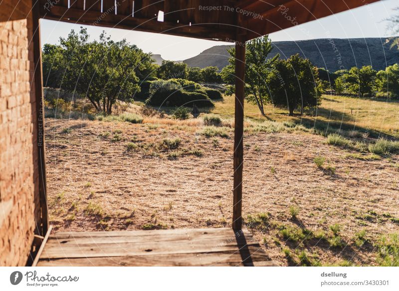 Wooden veranda of a brick house in the evening light Calm straightforwardness Ghost town Sun Deep depth of field Loneliness Old Brown Back-light Tracks