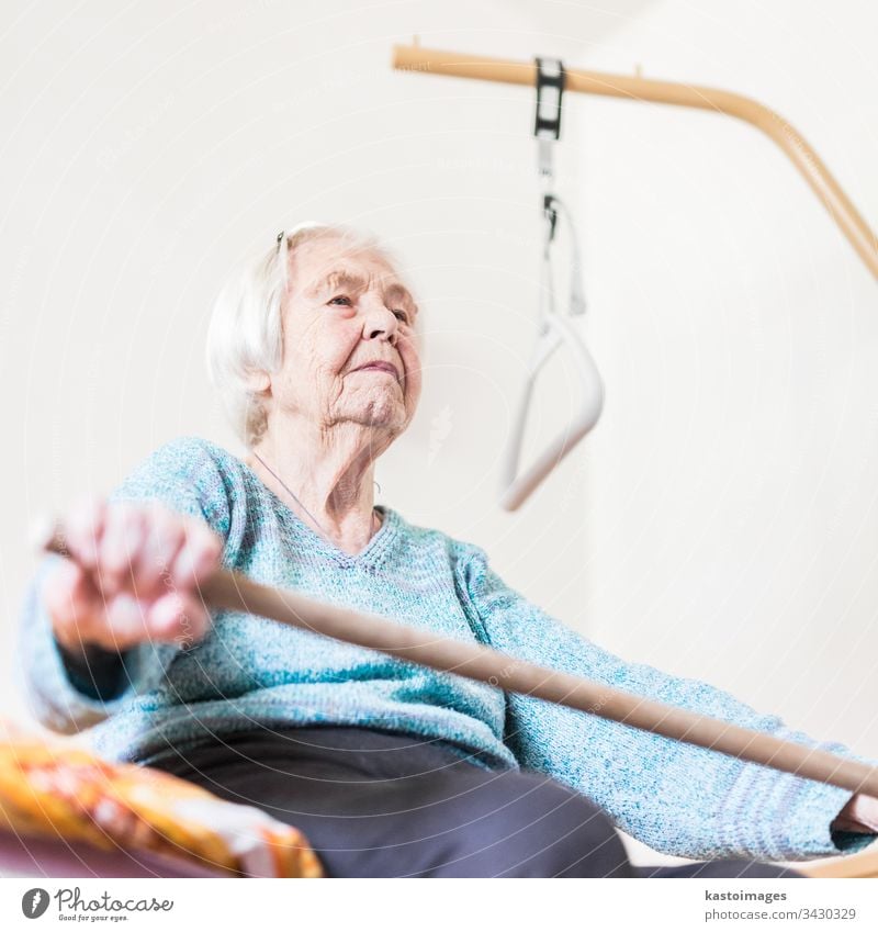 Elderly 96 years old woman exercising with a stick sitting on her bad. health care senior geriatric workout home bed patient happy social pensioner retirement