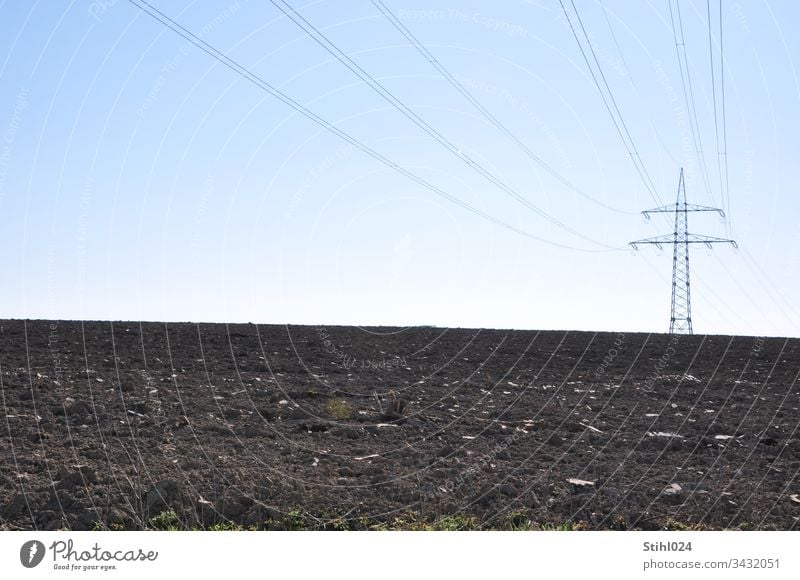 High voltage pylon stands lonely at a distance on a ploughed field Electricity pylon stream power supply acre Plowed Agriculture Horizon Winter Lonely