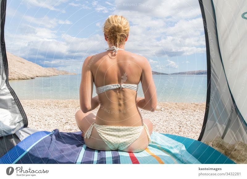 Rear view of beautiful young caucasian woman enjoying summer sun on Mediterranean beach protected from heat and sunburns by shade tent. beauty lifestyle ocean