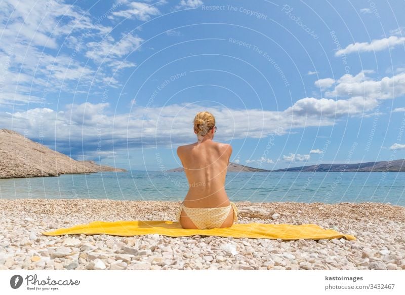 Rear view of sexy young caucasian woman sunbathing topless on romote pabble beach on Pag island, Croatia, Mediterranean. summer body tanning vacations beauty