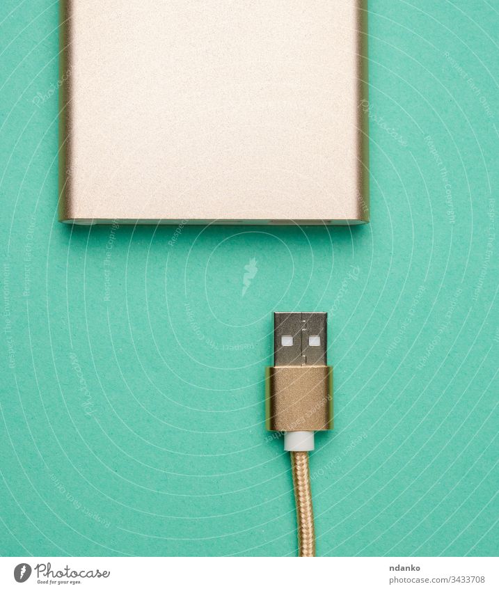 golden power bank and cord with a usb connector for recharging mobile devices on a green background cable charger energy technology battery digital plug