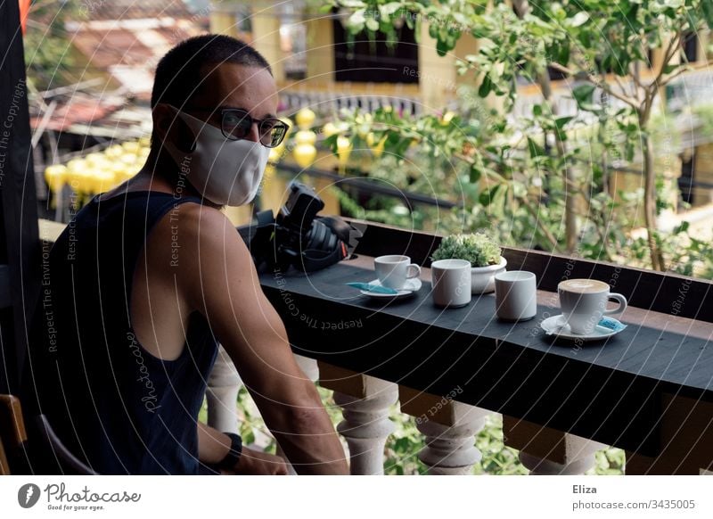 A man with a face mask is sitting in a café abroad, where he is stranded because of the corona virus COVID covid-19 Foreign countries Man Tourist Life vacation