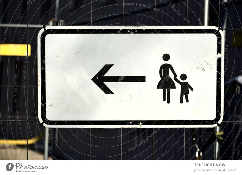 A white sign for pedestrians with a black pictogram on a barrier grille, signalled by an arrow to a stylised woman with a small child on her hand: Keep going left. | Corona Thoughts