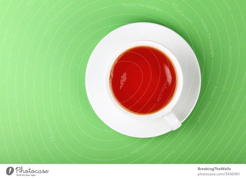 White cup of black or red fruit tea over green background Tea infusion white saucer paper pastel closeup elevated top view high angle directly above hot drink