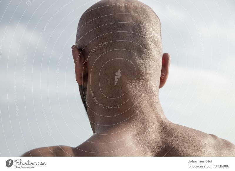 Male back of the head in front of a blue sky in rear view Bald or shaved head Man masculine Skin hair Facial hair ears Back Shoulder Back of the head Head