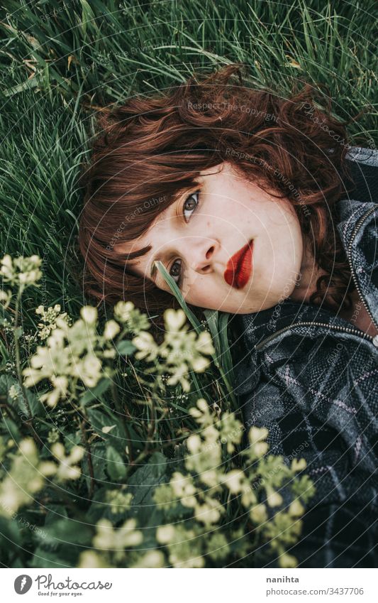 Young beautiful woman resting in a field of flowers portrait mood spring dark romantic nostalgia emotions green brunette pretty face white caucasian nature