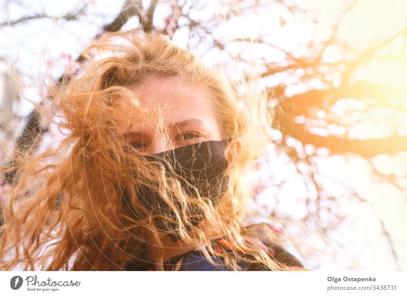 Girl in a medical mask on a background of flowering trees. The mask is black. Protection against virus, flu. Spring allergy protection spring recovery illness