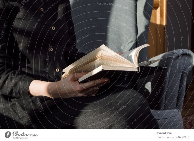 Closeup of woman in black dress holding book on her lap, selective focus books chair cozy faceless female fingers hands hobby home hygge leisure lifestyle