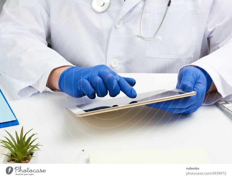 doctor in a white medical coat sits at a table and holds an electronic tablet in his hand, touches the screen with his right hand health stethoscope technology