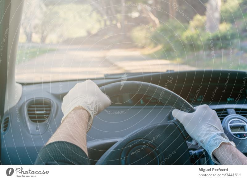 Hands holding the steering wheel of a car while driving with latex gloves to avoid contagion adult auto automobile car interior control coronavirus dashboard