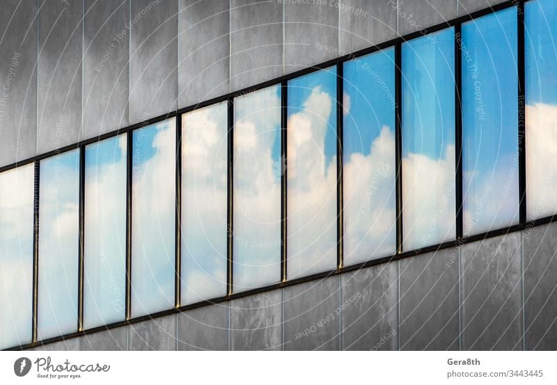 reflection of blue sky and white clouds in the windows of a gray concrete building abstract architecture background blocks business city diagonal empty fragment