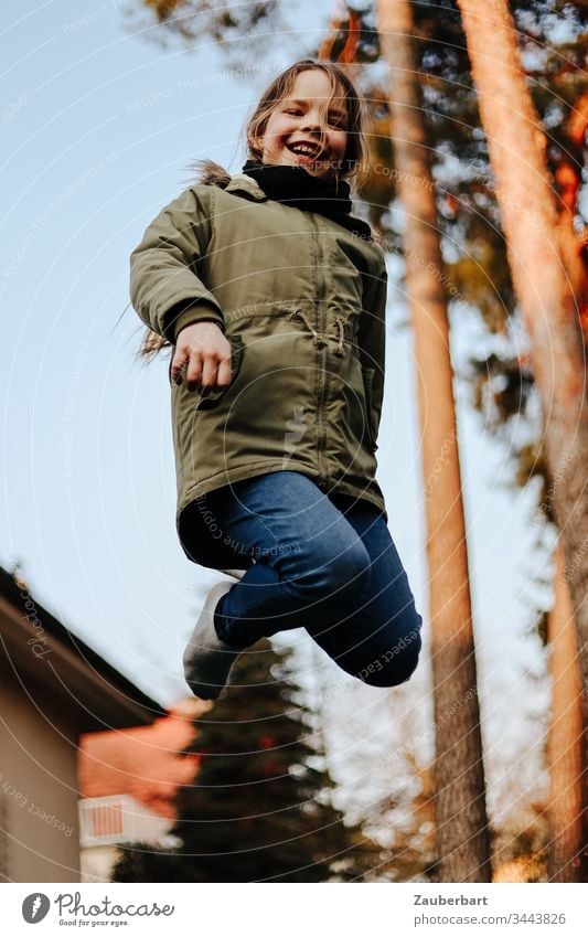Little girl in flight, she jumps on a trampoline in the garden in front of two pines Small Child Schoolchild Trampoline Hop Jump Flying Garden Joy Playing