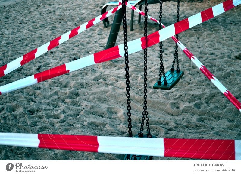 Corona-Thoughts | Red and white signal crime scene flutter tape stretched criss-cross over a children's swing and the sand of a children's playground