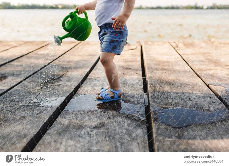 A small girl is playing with a watering can of a wooden bridge. Spring and summer. Gardening. green watering can baby little child cute garden background white